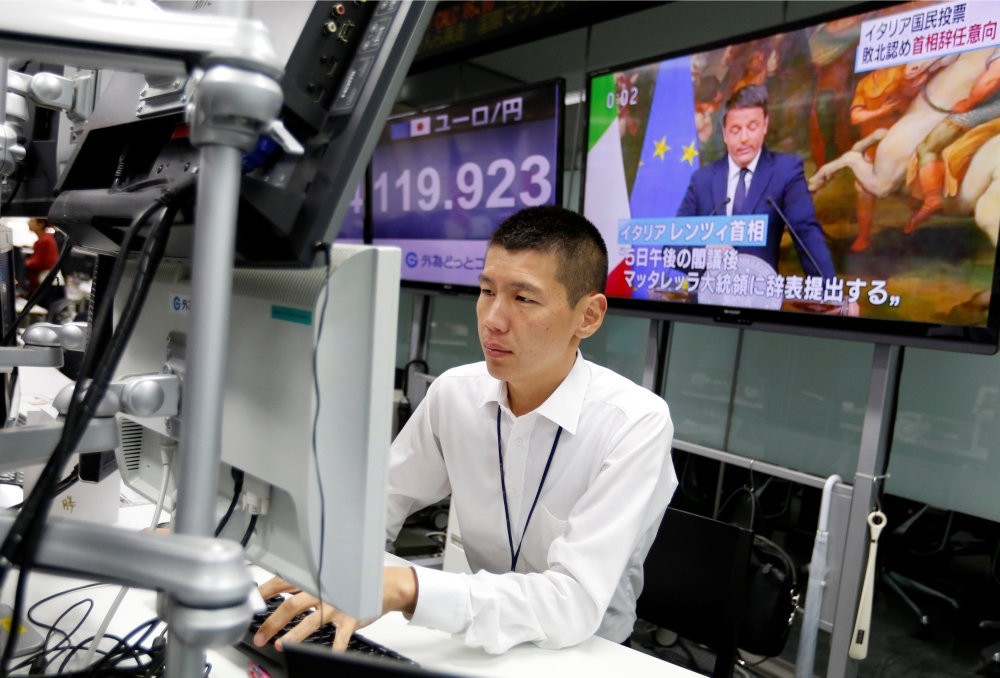 An employee of a foreign exchange trading company works in front of monitors showing Italian Prime Minister Matteo Renzi on TV news, and the Japanese yen's exchange rate against the euro in Tokyo, Japan.