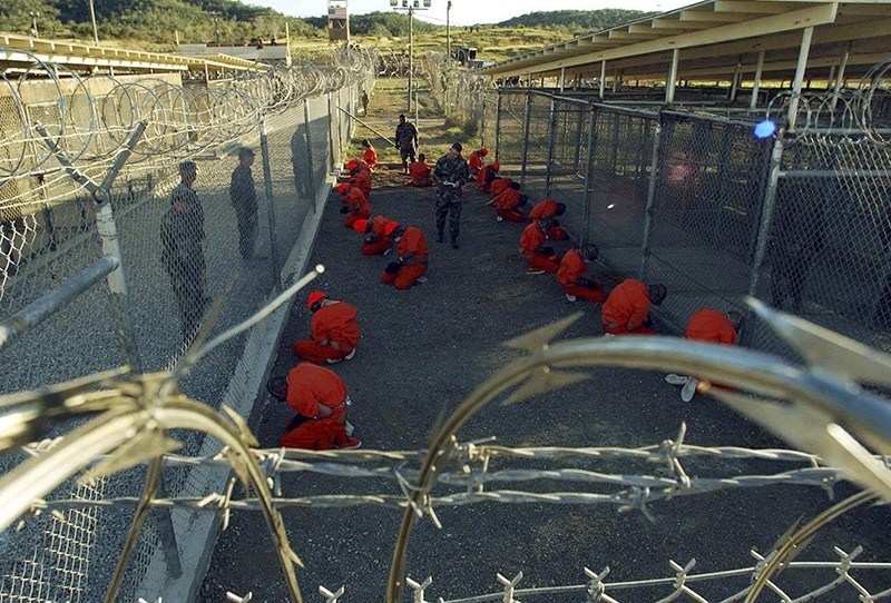 In this file photo, detainees in orange jumpsuits sit in a holding area under the watchful eyes of military police during in-processing to the temporary detention facility at Camp X-Ray of Naval Base Guantanamo Bay. (Reuters Photo)