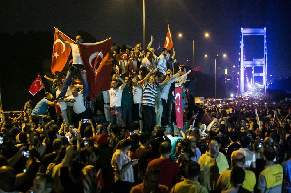 A large group of people denouncing the coup attempt on an abandoned tank, holding Turkish flags on the July 15 Martyrs' Bridge (Bosporus Bridge).