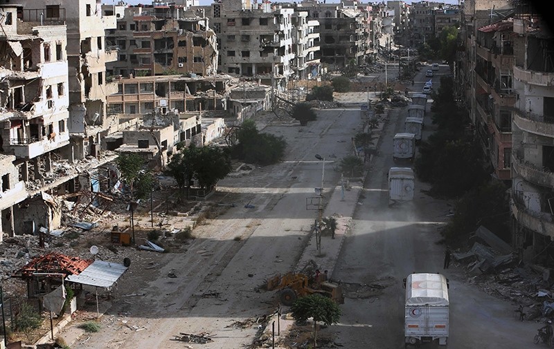 A convoy of Syrian Red Crescent trucks carrying aid drives amidst destruction in Harasta, a besieged rebel-held suburb of Syria's capital Damascus, on June 19, 2016 (AFP Photo)