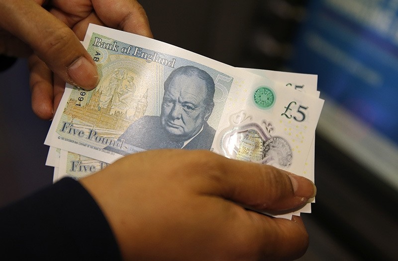 Amanda a member of staff at a branch of Halifax bank, in London, displays the new British 5 pound sterling notes, made from polymer, which were launched Tuesday, Sept.13, 2016. (AP Photo)