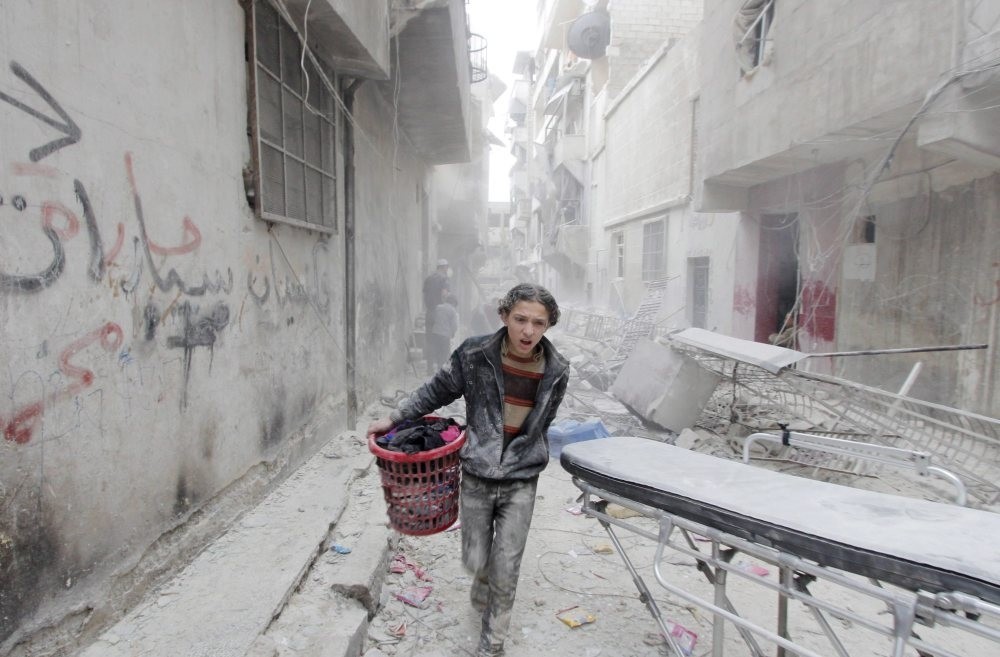 A boy carries his belongings at a site hit by a barrel bomb dropped by the Assad regime in Aleppo's al-Fardous district. (Reuters Photo)