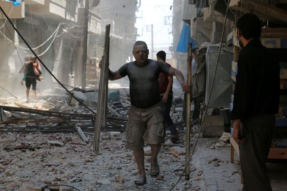 A Syrian man covered with dust carries pieces of metal on a street cluttered with rubble following an airstrike on the rebel-held neighborhood of Sakhur in Aleppo.
