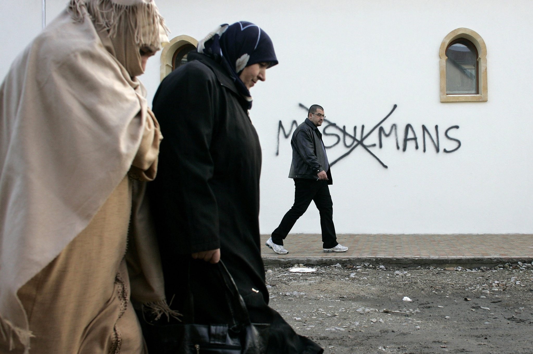In this Monday Feb. 8, 2010 file photo, Muslim residents walk past racial slurs painted on the walls of a mosque in the town of Saint-Etienne, central France. (AP Photo)