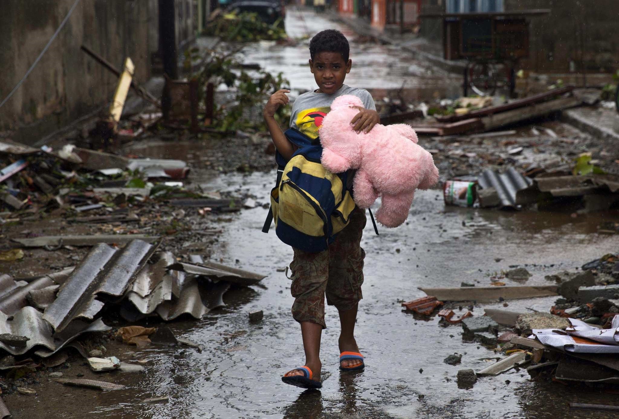 A boy walks, carrying a backpack and a teddy bear, through a street littered with debris the morning after Hurricane Matthew drove across Baracoa, Cuba, Wednesday, Oct. 5, 2016. (AP Photo)