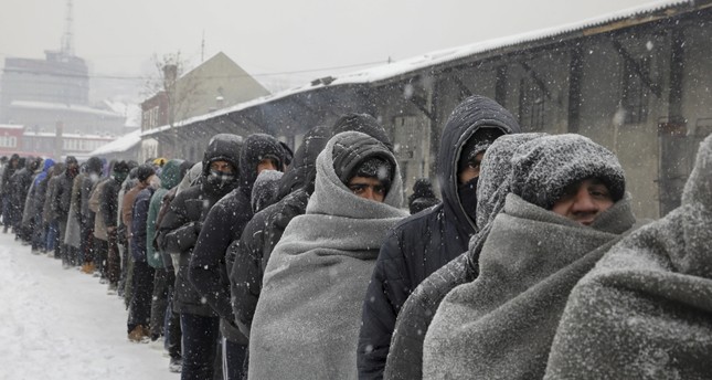 Refugees wait in line to receive a plate of free food during a snowfall outside a derelict customs warehouse in Belgrade, Serbia, Jan. 11.