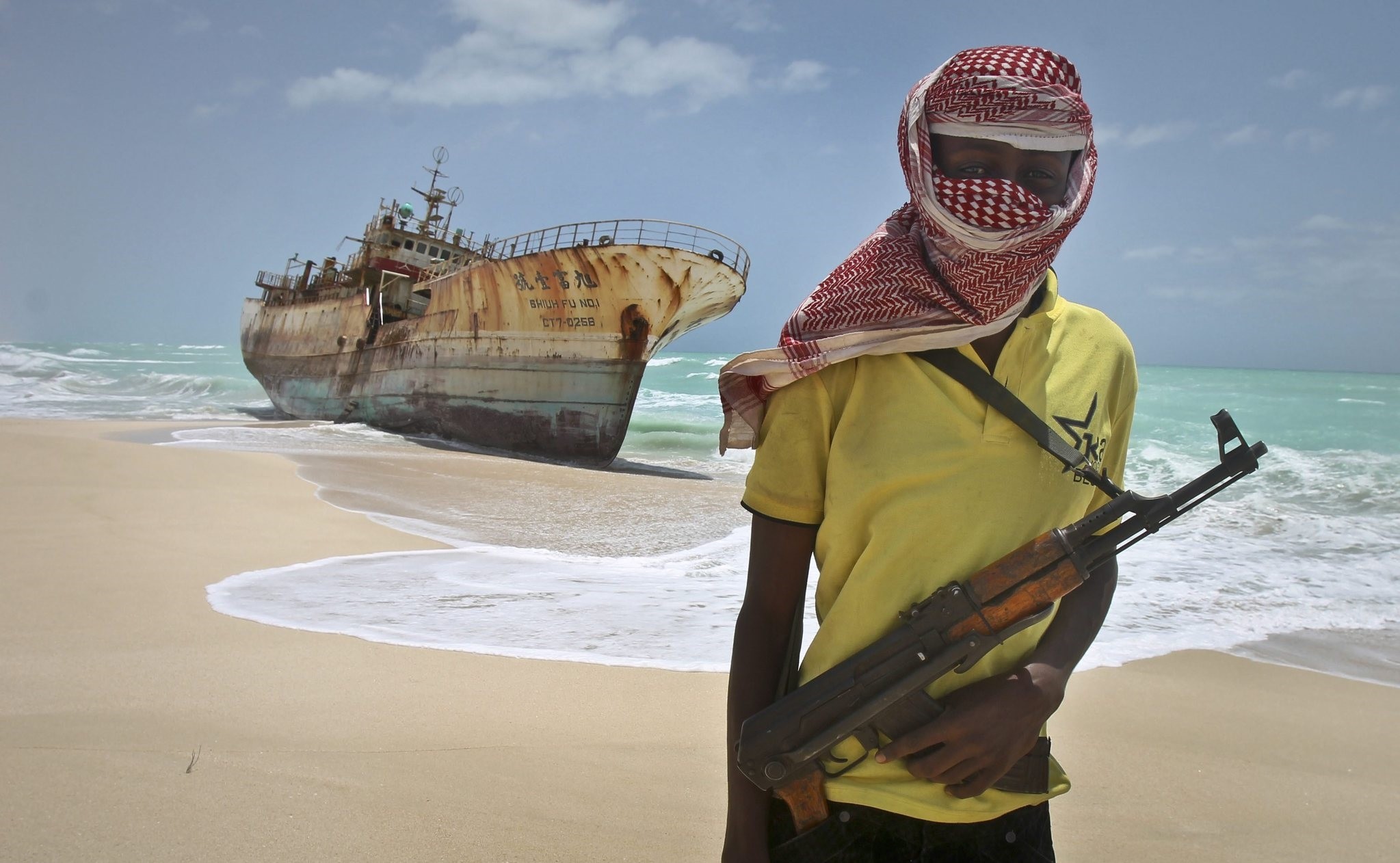 In this Sunday, Sept. 23, 2012 file photo, masked Somali pirate Hassan stands near a Taiwanese fishing vessel that washed up on shore after the pirates were paid a ransom and released the crew. (AP Photo)