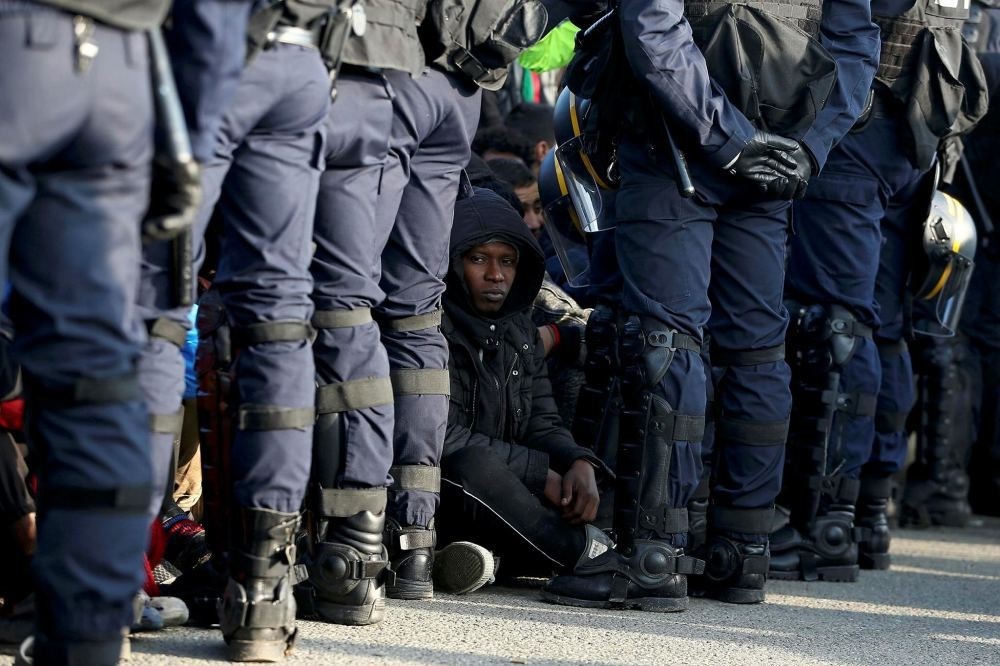 French police stand near as migrants wait in front of a processing center to be registered on the second day of their evacuation during the dismantlement of the camp called the ,Jungle, in Calais, France, Oct. 25.