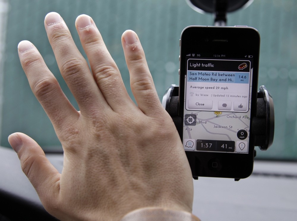 Ben Gleitzman waves his hand over a traffic and navigation app called Waze on his Apple iPhone in a Menlo Park, Calif., parking lot during a demonstration showing traffic conditions on the display.