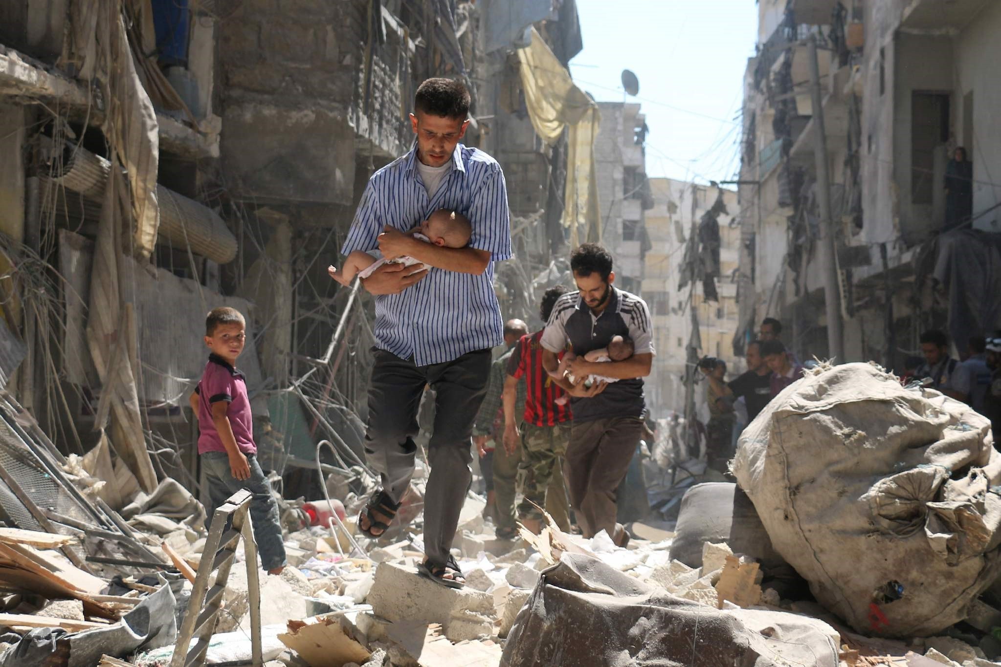Syrian men carrying babies make their way through the rubble of destroyed buildings following a reported air strike on Aleppo. (AFP Photo)