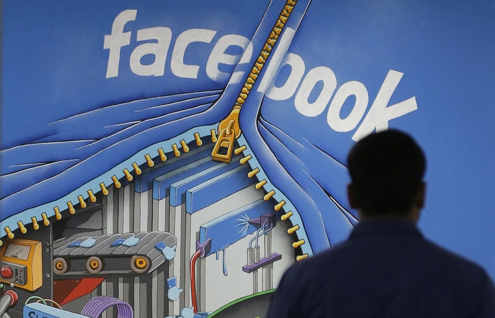 A Facebook employee walks past a sign at Facebook headquarters in Menlo Park, California.