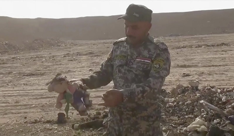 In this Monday, Nov. 7, 2016 frame grab from video, an Iraqi federal police officer holds a stuffed toy at the site of a mass grave in Hamam al-Alil, Iraq. (AP Photo)
