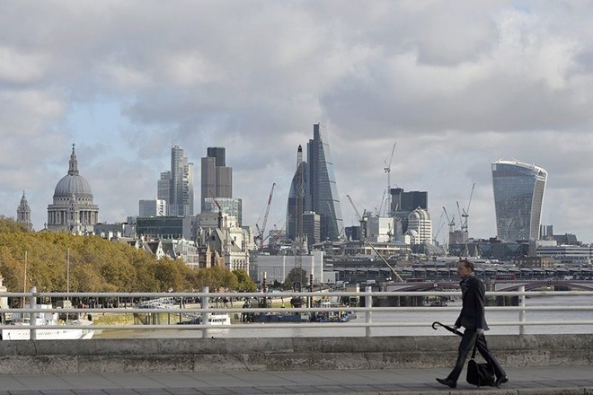 A man crosses Waterloo Bridge with the backdrop of the City of London and the financial district in London.