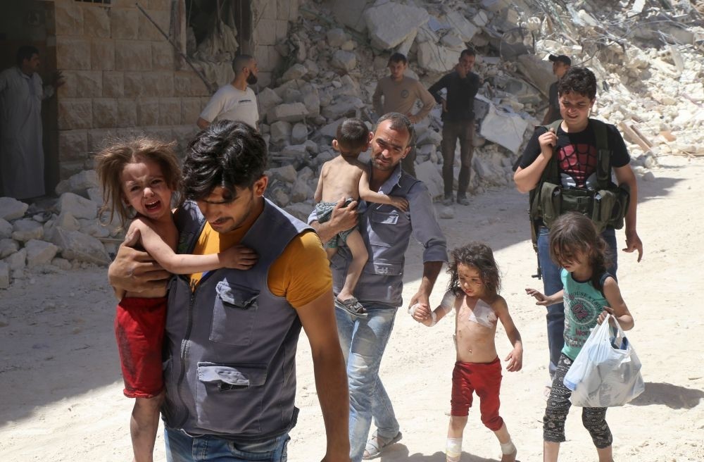 Syrian men carry injured children amid the rubble of destroyed buildings following reported airstrikes on the opposition-held neighborhood of al-Mashhad in the northern city of Aleppo on July 25.