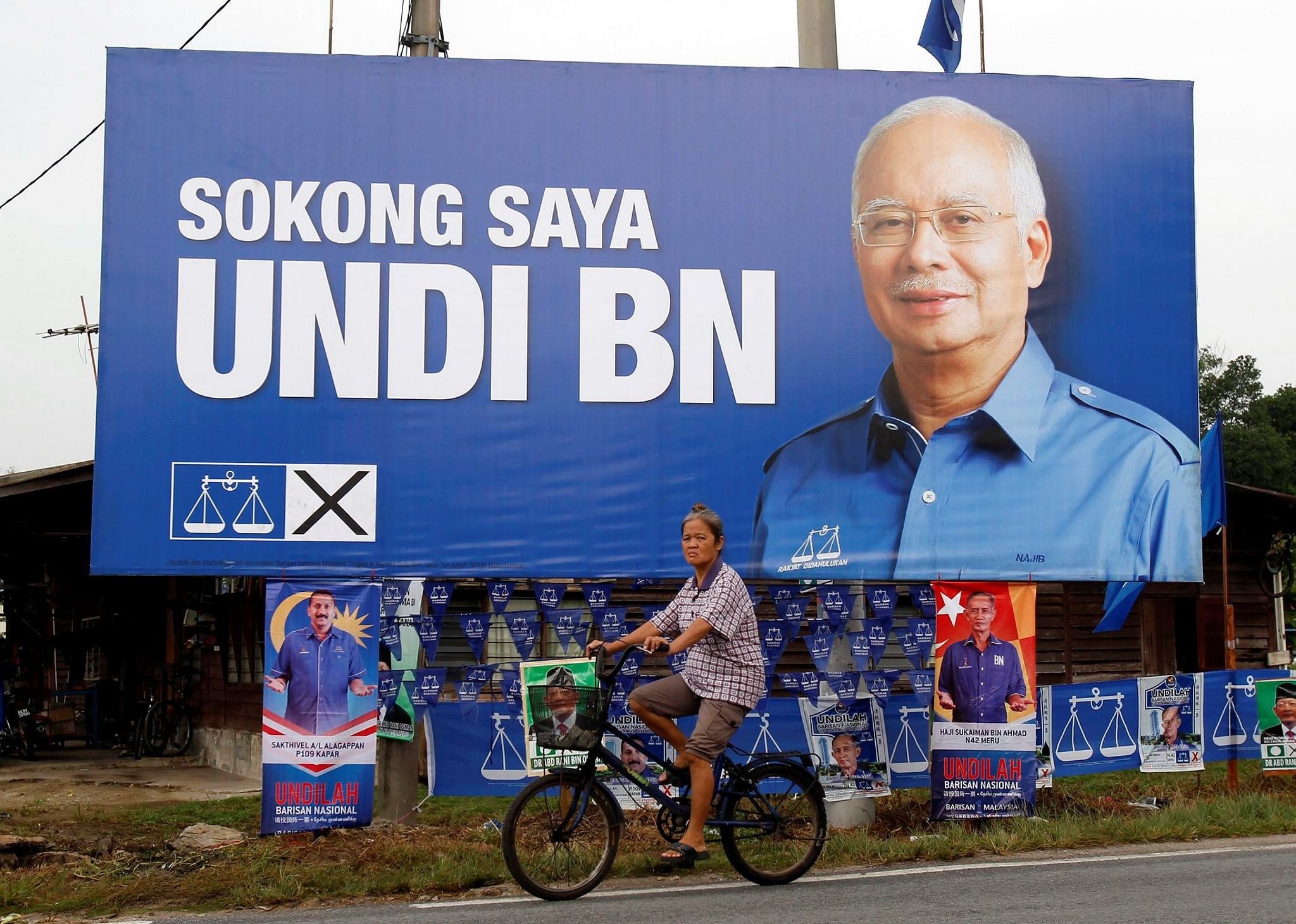 Malaysian ethnic Chinese woman rides past a billboard of Malaysia's ruling National Front coalition with a portrait of Prime Minister Najib Razak which translates ,I vote for National Front coalition, (AP Photo)