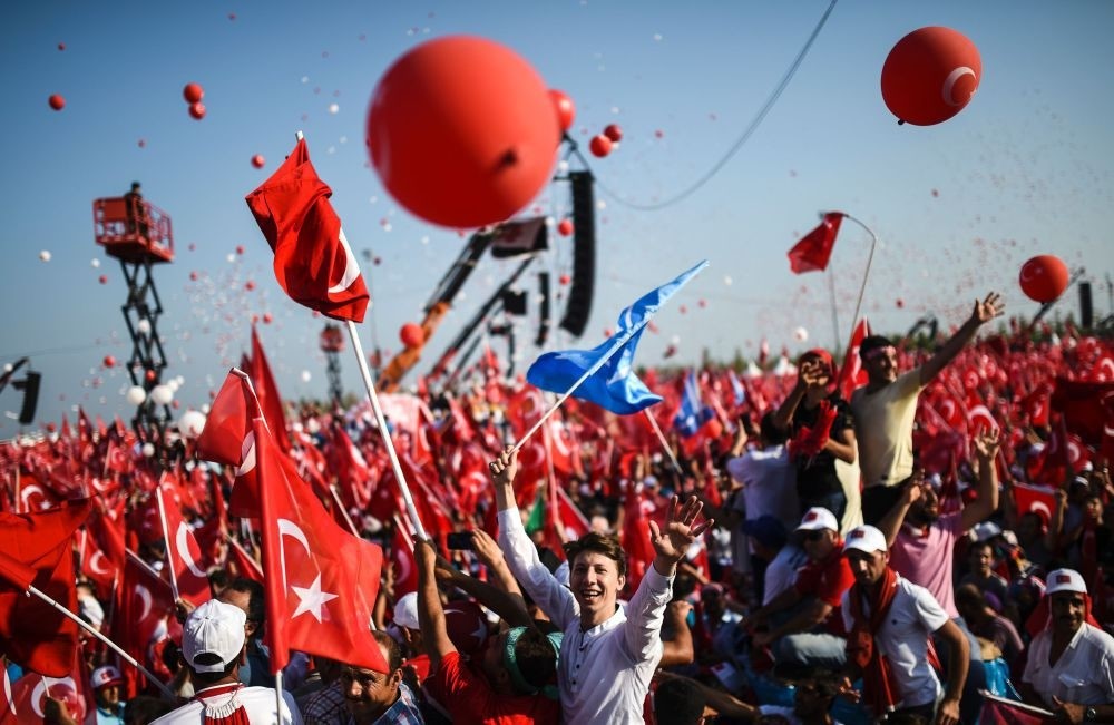 People waving flags as they stand in front of giant screens next to balloons in the color of the Turkish national flag in Istanbul at the Democracy and Martyrs Rally against the July 15 coup attempt, Aug. 7.