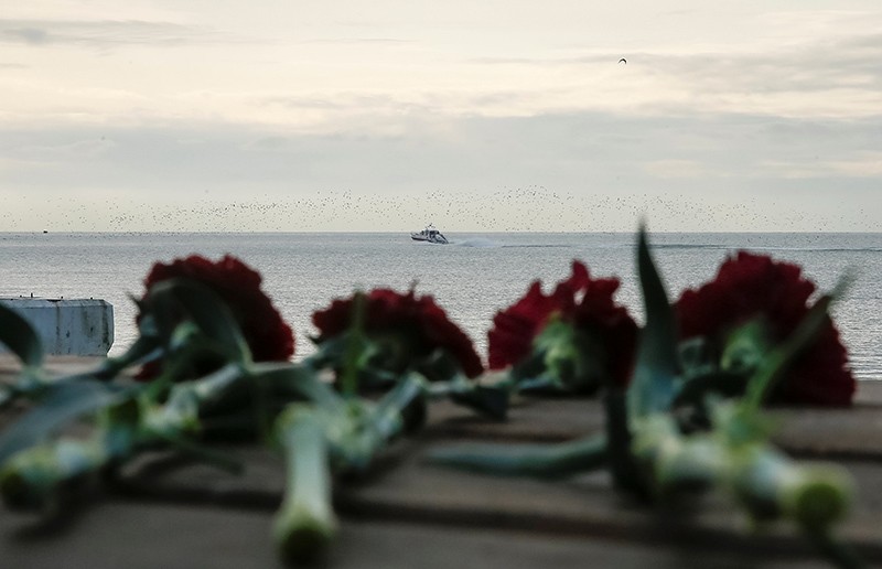 Flowers are placed on a pier as a boat of Russian Emergencies Ministry sails near the crash site of a Russian military Tu-154 plane, which crashed into the Black Sea on its way to Syria on Sunday (Reuters Photo)