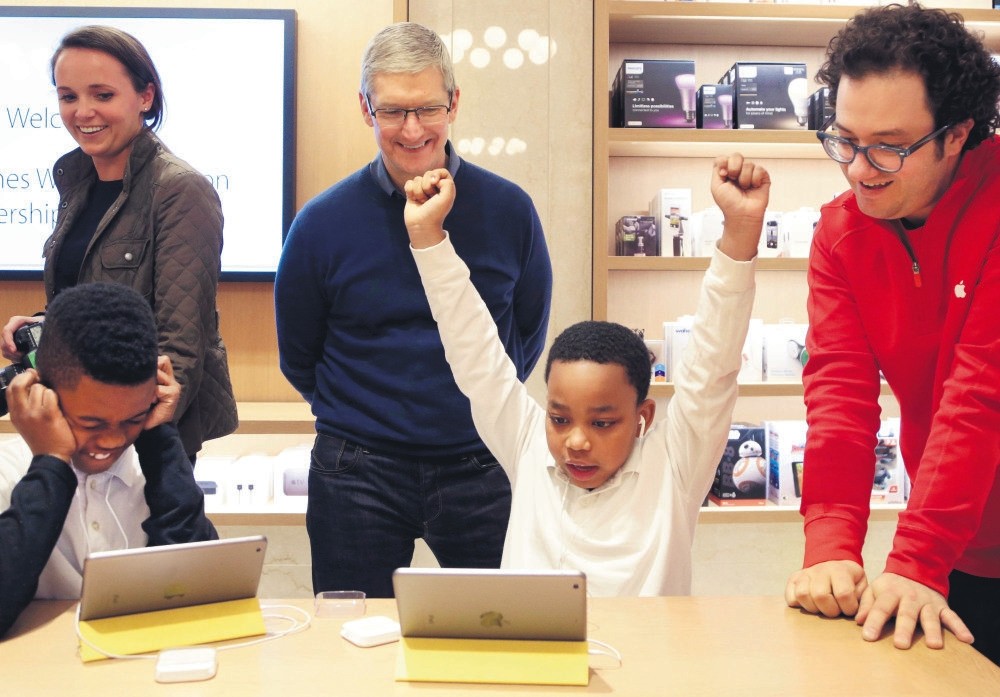 Jaysean Erby raises his hands as he solves a coding problem as Apple CEO Tim Cook watches from behind at an Apple Store, in New York