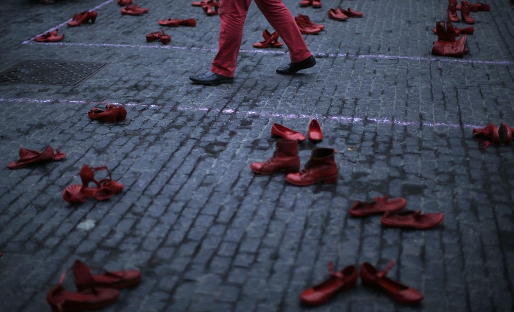 A man walks between red shoes displayed as part of a protest to highlight violence against women at the Sant Jaume square in Barcelona.
