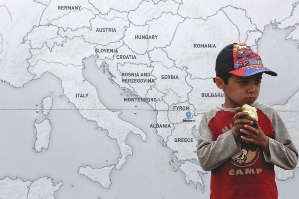 A boy eats an apple next to a map illustrating part of Europe at a makeshift camp for refugees and migrants at the Greek-Macedonian border near the village of Idomeni, Greece.