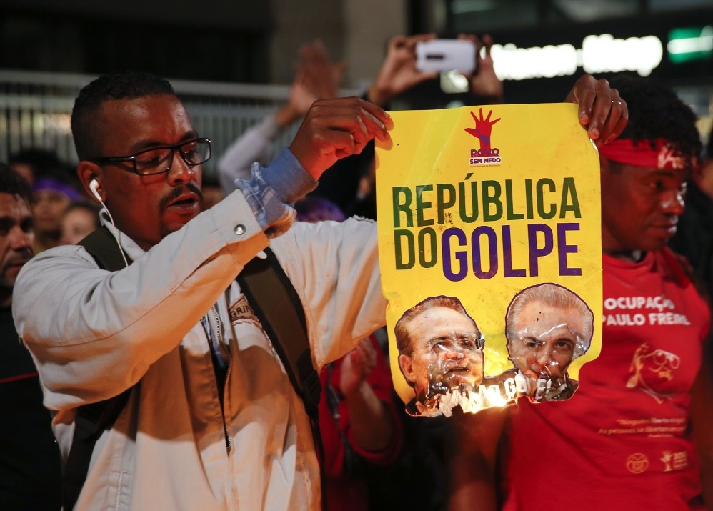 A demonstrator set fire to a poster that reads: ,Coup Republic,, during a protest in support of Brazil's suspended President Rousseff.