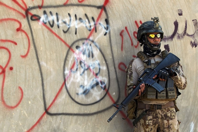 An Iraqi soldier stands next to a wall with a red cross above a slogan of the Daish terrorist group. (AFP Photo)