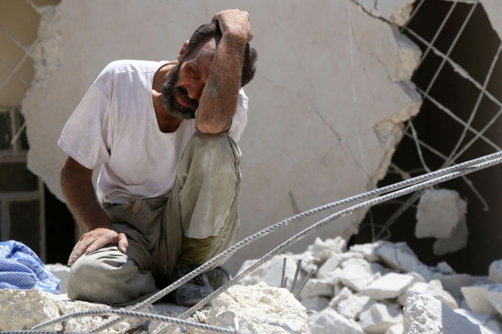 A man looks on as Syrian civil defense workers look for survivors under the rubble of a collapsed building following reported airstrikes on July 17 in the opposition-controlled neighborhood of Karm Homad in the northern city of Aleppo.