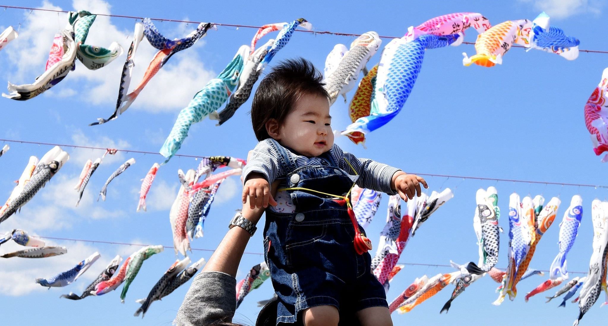 A father holds up his baby under carp streamers fluttering in a riverside park in Sagamihara, suburban Tokyo, on April 29, 2016 ahead of May 5 Children's Day in Japan. (AFP Photo)