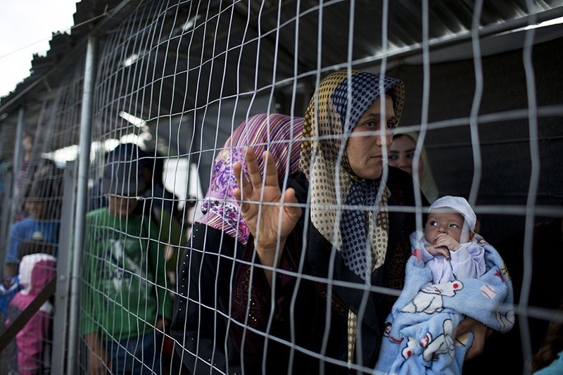 Syrian woman holds 9 days old baby who was born in the camp as refugees  queue to receive food at the northern Greek border point of Idomeni, Greece, May 10, 2016. (AP)