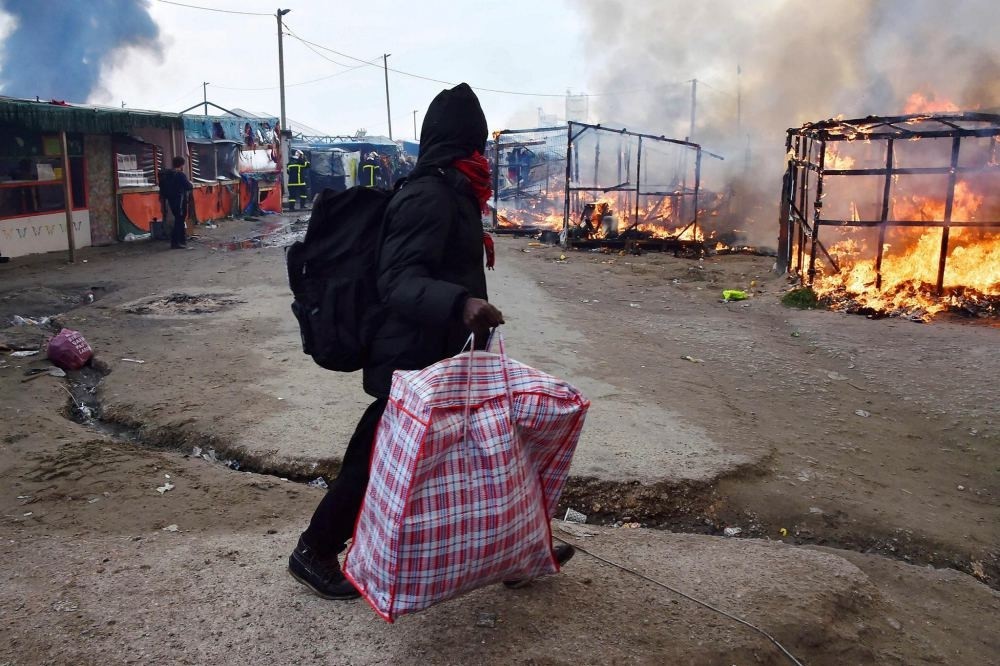 A migrant carrying his bags as he walks by makeshift shelters on fire at the ,Jungle, migrant camp in Calais, northern France, on Oct. 26.