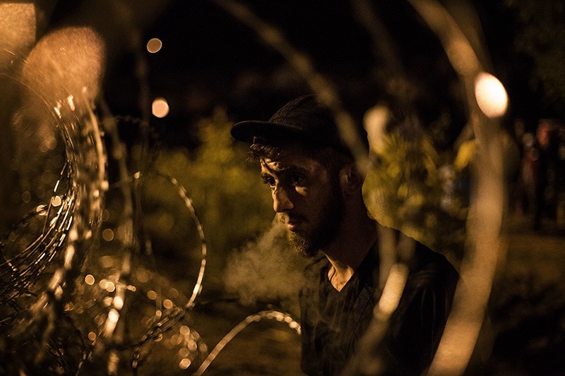  A Syrian refugee looks at Hungarian riot police from the Serbian side of the fence built by Hungarian authorities at the border between Serbia and Hungary, in Horgos, Serbia, Sept. 16, 2015. (AP Photo)