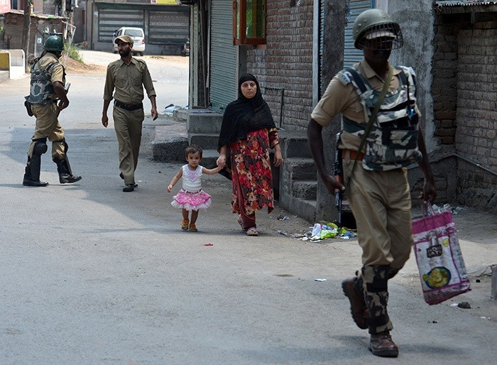 Indian paramilitary troopers patrol as a Kashmiri woman with a child walks during a curfew in Srinagar on August 5, 2016. (AFP Photo)