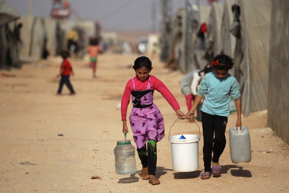 Internally displaced Syrian girls carrying water containers in Jrzinaz camp, south Idlib, Syria, June 21, 2016.
