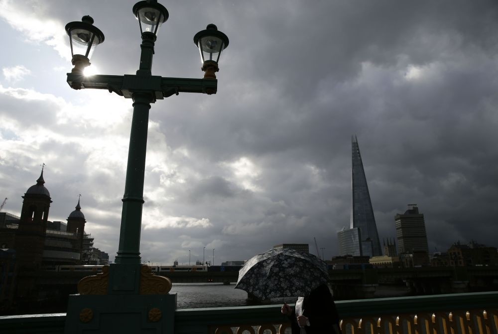 A lone commuter takes shelter from the rain beneath her umbrella as she heads to the City of London across Southwark Bridge in front of the Shard skyscraper in central London on June 27, 2016. 