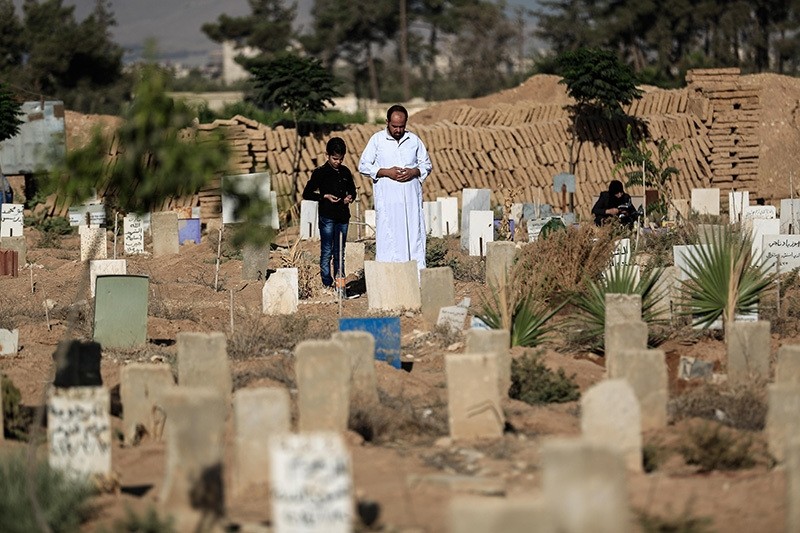 A Syrian man and his son pray over the grave of a relative at a cemetery in the rebel-held town of Douma, east of the capital Damascus, on September 12, 2016, on the first day of the Muslim holiday of Eid al-Adha. (AFP Photo)