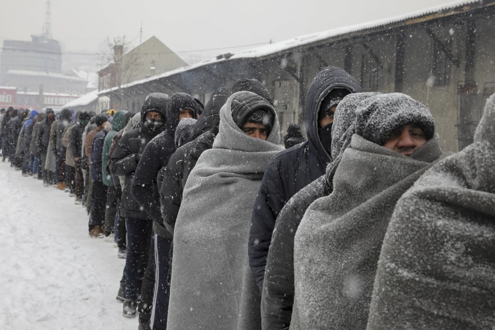 Refugees wait in line to receive a plate of free food during a snowfall outside a derelict customs warehouse in Belgrade, Serbia, Jan. 11.