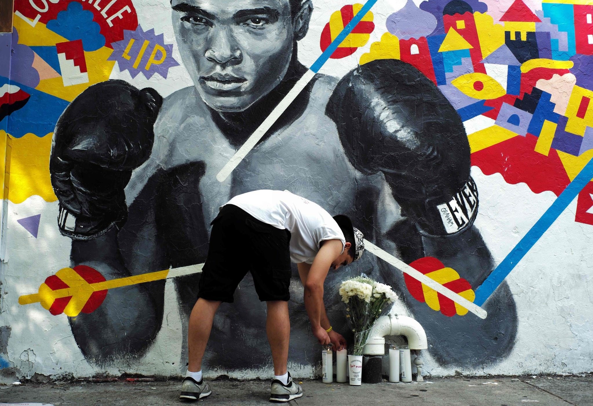 A man places a candle under a mural of the late boxer Muhammad Ali in New York on June 4, 2016 (AFP Photo)