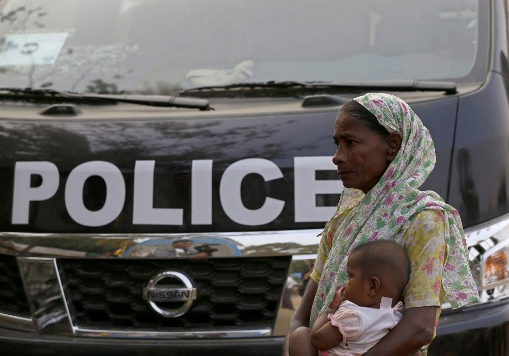 A Muslim woman carries her child as she stands near a police vehicle at the NgaKhuYa village near the Maungdaw town of Bangladesh-Myanmar border, Rakhine State, western Myanmar.