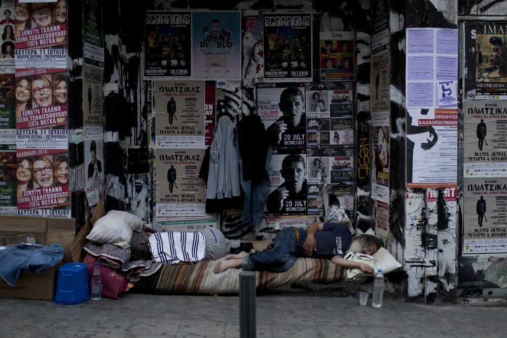 Two homeless men sleep outside the entrance of a boarded up store in central Athens . 