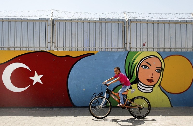A child cycles past graffiti at the Oncupinar camp for Syrian refugees next to the border crossing with Syria, near the town of Kilis in southeastern Turkey, Monday. (AP Photo)