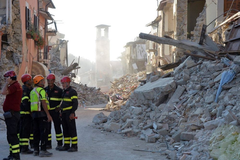 Firefighters and rescue workers stand near the damaged Santu2019Agostino church (C) and rubble and debris of damaged buildings.