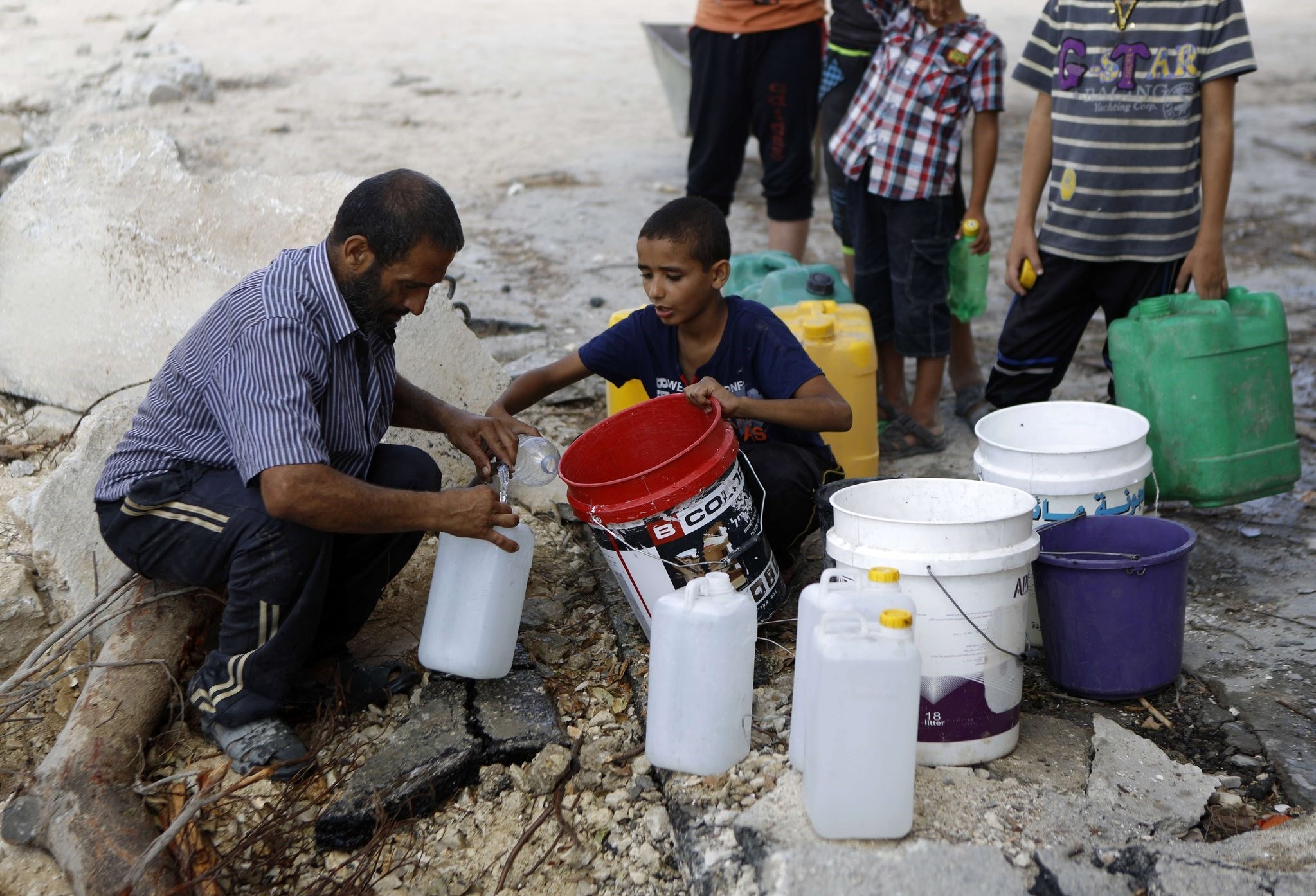 A Palestinian man and children fill containers with water from a broken main in Gaza City's al-Shejaea neighborhood on August 6, 2014 (AFP Photo)