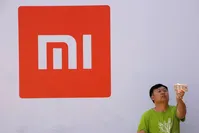 A man takes a selfie in front of the Xiaomi logo.