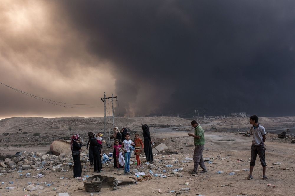 Iraqi villagers gather on a road as smoke rises from the Qayyarah area, southern Mosul, Oct. 19, 2016, during an operation against Daesh terrorists to retake the main hub city.