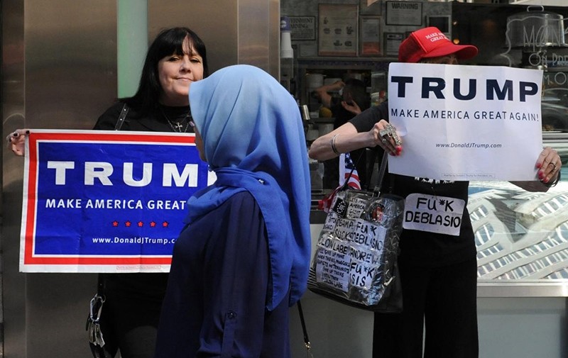A woman wearing a Muslim headscarf walks past people holding U.S. Republican presidential nominee Donald Trump (Reuters Photo)