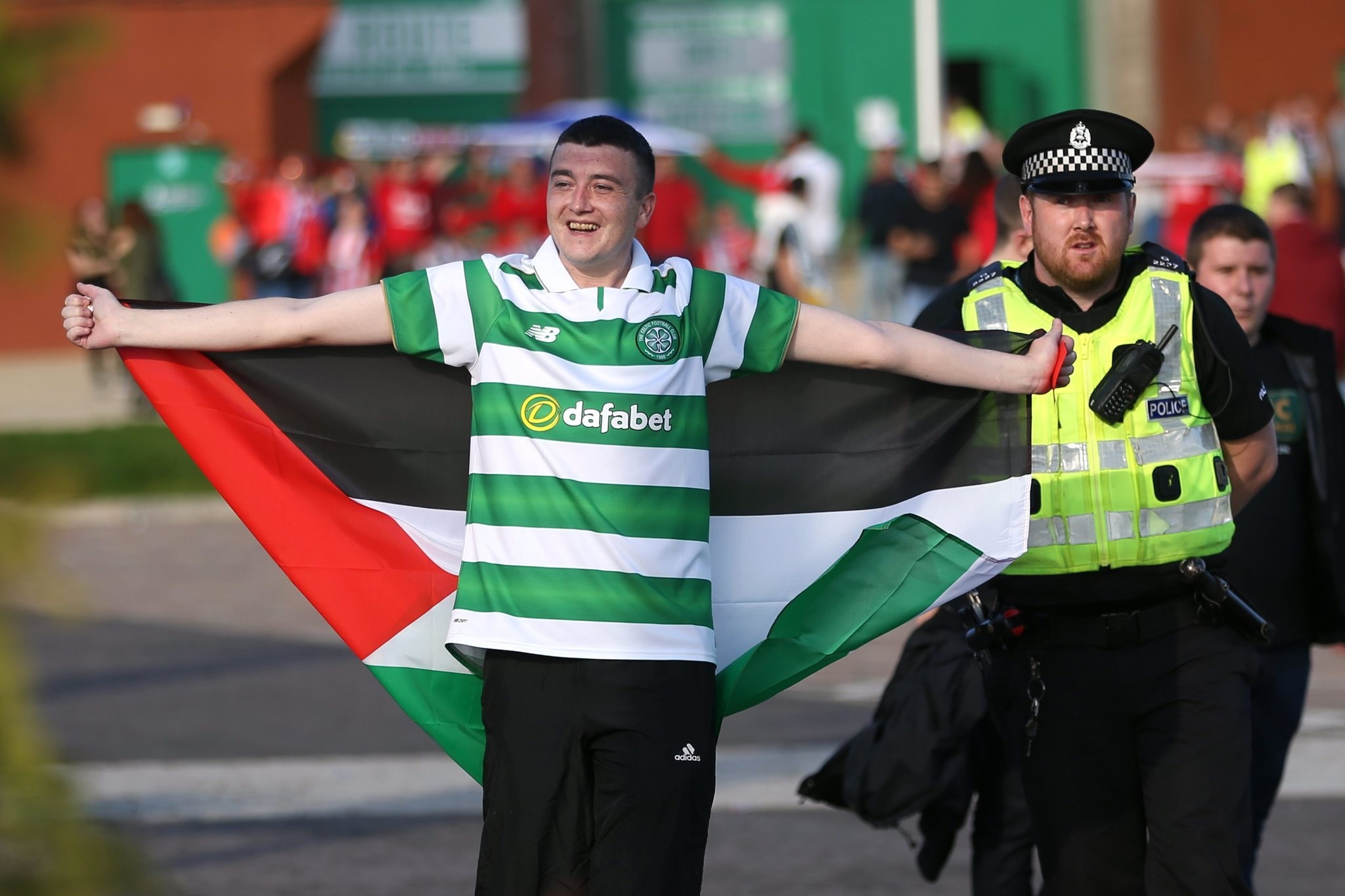 A Celtic fan with a Palestinian flag is escorted by a Police officer away from Hapoel Beu2019er-Sheva fans outside the stadium before the match. (REUTERS Photo)