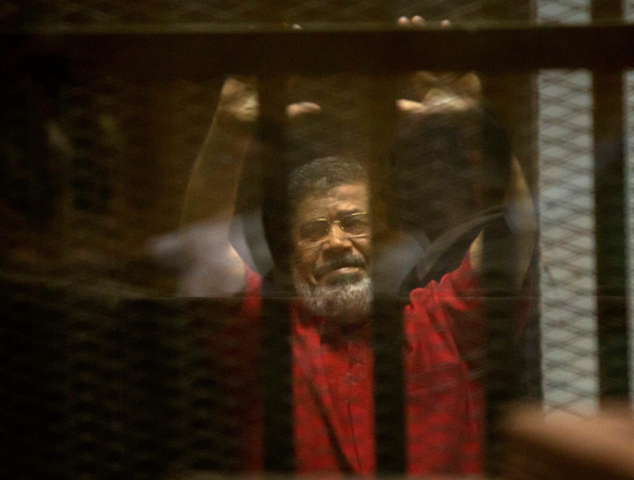 Former Egyptian President Mohammed Morsi raises his hands inside a defendants cage in a makeshift courtroom at the national police academy, in an eastern suburb of Cairo, Egypt, Saturday, June 18, 2016. (AP Photo)
