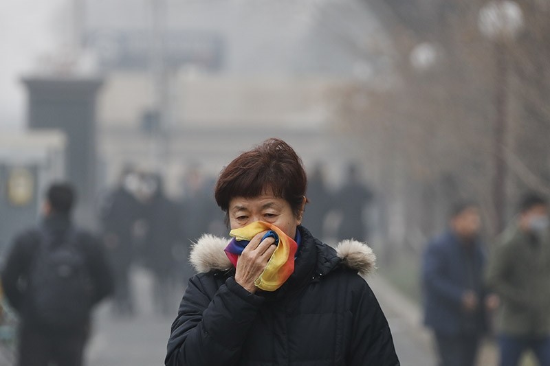 A woman uses a scarf to cover her mouth for protection against the air pollution as she walks on a street in Beijing, China in Dec. 2016. (AP file photo)
