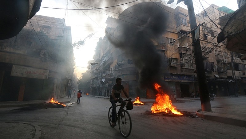 A man rides a bicycle past burning tyres, which activists said are used to create smoke cover from warplanes, in Aleppo, Syria August 1, 2016 (Reuters Photo)