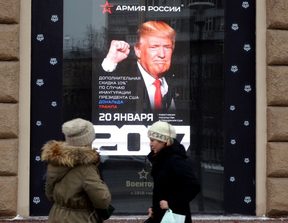 Women walk past a screen displaying a portrait of U.S. President-elect Donald Trump installed inside a Voentorg shop window in central Moscow